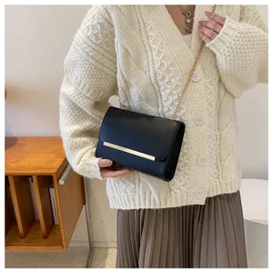 Chic black crossbody bag with gold hardware detail and chain strap worn by a model