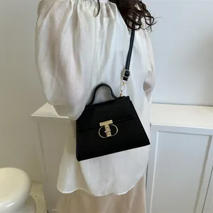 Borsa a mano in pelle nera minimalista con chiusura a T dorata indossata da modella