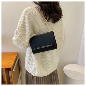 Detail of a chic black leather crossbody bag with a sleek gold metal bar and chain strap