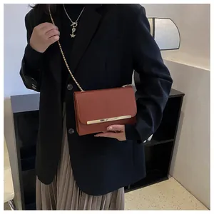 Detail of caramel leather flap bag with gold metal trim and chain strap on a model
