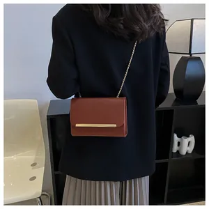 Detail of a brown leather crossbody bag with a gold metal bar and chain strap on a model