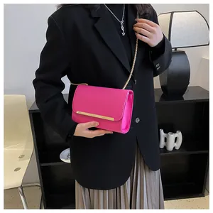 Close-up of fuchsia flap crossbody bag with gold chain and metal bar on black blazer