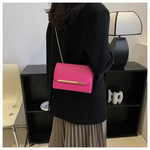 Bright pink crossbody chain bag with gold metal trim worn over a black blazer