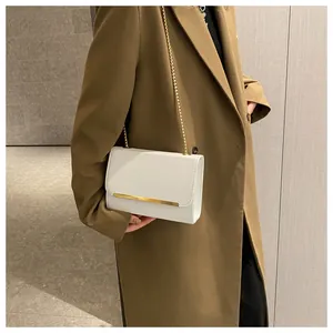 Close-up of white crossbody bag with gold chain strap on stylish brown trench coat