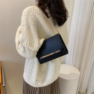 Sac bandoulière noir minimaliste avec chaîne dorée porté par un mannequin en tenue décontractée