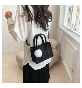 Detail einer kleinen schwarzen Stepphandtasche mit weißem flauschigem Pompon am Model