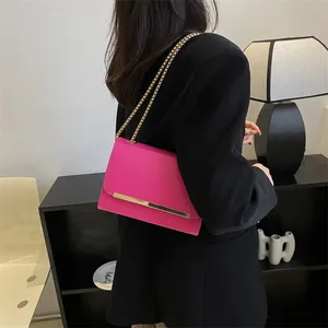 Chic rose pink chain shoulder bag with gold metal bar accent on a black suit blazer
