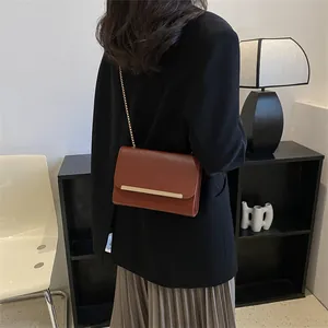 Minimalist brown chain crossbody bag with golden metal trim shown on a model in a blazer