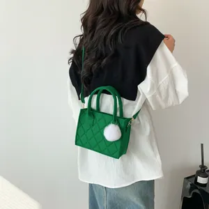 Grüne gesteppte Filztasche mit Plüschpompon und Gurt, getragen von einem Modell