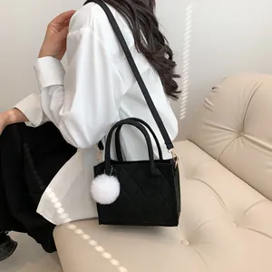 Schwarze Stepptasche mit Rautenmuster und weißem Kunstpelz-Anhänger am Schultergurt