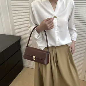 Vintage dark brown leather baguette bag with gold buckle worn by model in chic outfit