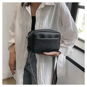 Détail du sac bandoulière en cuir noir avec une sangle en tissu à rayures tendance