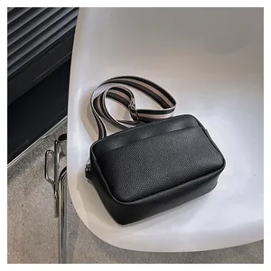 Détail du sac bandoulière en cuir noir avec une large sangle en tissu rayé