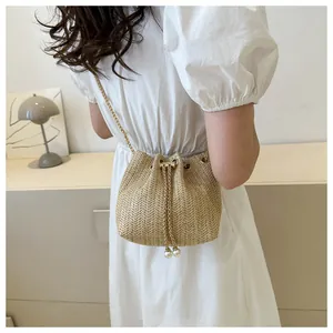 Detail of straw woven bucket bag featuring gold chain strap and pearl drawstring accents