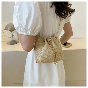Detail of straw bucket bag with gold chain strap and pearl drawstring tassels