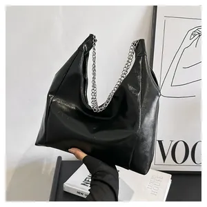 Détail d'un sac cabas noir brillant avec une bandoulière à grosse chaîne argentée élégante