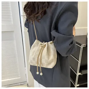Detail of cream bucket bag featuring checkerboard texture and pearl drawstring accents
