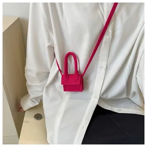 Detail of rose red micro crossbody bag worn by model over a white shirt and black pants