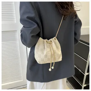 Detail of cream bucket bag featuring checkered texture, gold chain and pearl drawstring