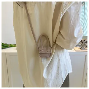 Detail view of a minimalist beige mini lipstick bag with slim crossbody strap on model