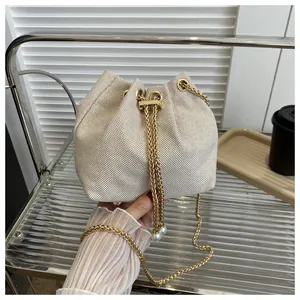 Detail of cream canvas bucket bag featuring a drawstring closure and pearl chain strap