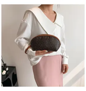Dettaglio di una pochette marrone stampata con cinturino in pelle tenuta da una modella