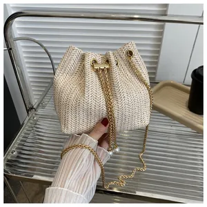 Close-up of beige woven bucket bag with pearl pendant detail and gold chain strap