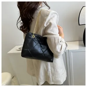 Détail du sac bandoulière noir matelassé avec chaîne dorée porté sur un blazer beige