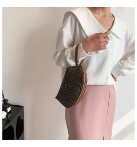 Dettaglio di una pochette a mezzaluna marrone con monogramma e manico in pelle e zip