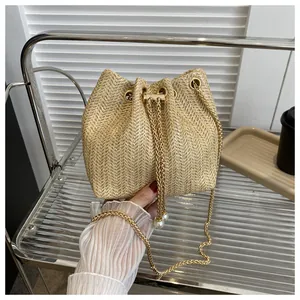 Detail of woven straw bucket bag featuring pearl drawstring and gold chain strap
