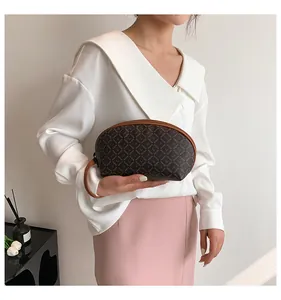 Dettaglio di una pochette a semicerchio marrone con monogramma tenuta da una modella
