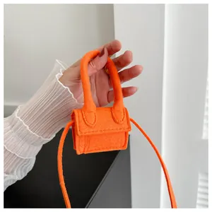 Macro shot of a tiny bright orange felt accessory bag held between two fingers