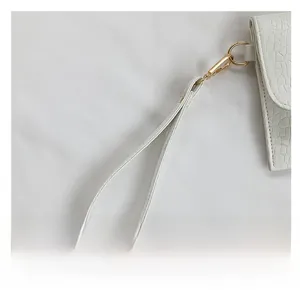 Detail view of white stone-patterned handbag with light gold metal hook and wrist strap