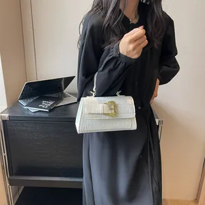 White faux crocodile skin top handle bag with vintage gold buckle held by a model