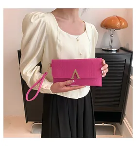 Detail of fuchsia crocodile texture envelope clutch bag with gold V-shape buckle and wristlet