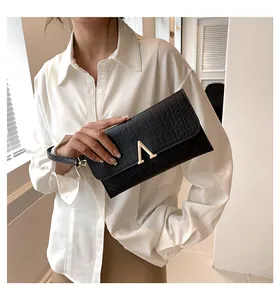Close-up of black crocodile-embossed envelope clutch with a gold V-shaped metal lock