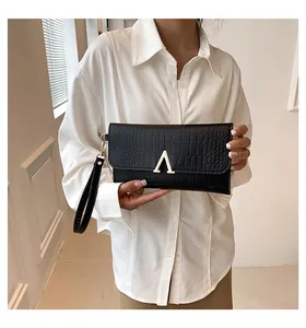 Detail of black faux crocodile leather clutch featuring a gold V-shaped metal buckle and wristlet