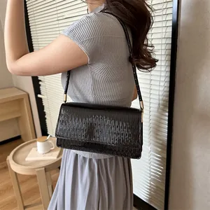 Borsa a spalla nera minimalista con dettagli dorati, indossata da una modella in luce