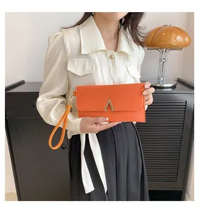 Detail of orange crocodile pattern envelope bag with gold V buckle on a female model