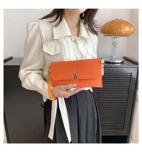 Chic orange envelope clutch bag with crocodile texture and metal logo in lifestyle setting
