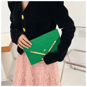 Detail of green crocodile texture envelope clutch bag with V-shaped gold metal trim