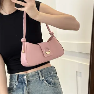 Pink minimalist underarm shoulder bag with gold clasp and knotted strap shown in use