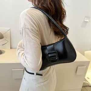 Minimalist black leather underarm bag with a crescent shape and square buckle detail