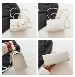 Detail view of white crocodile embossed square handbag with golden metal buckle and straps