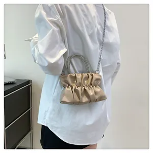 Detailed view of beige pleated cloud bag with luxury rhinestone-encrusted handle and chain