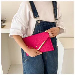 Fuchsia envelope clutch with crocodile texture and gold V-trim detail held by a model