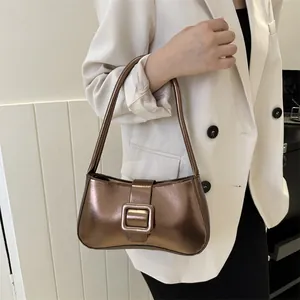Metallic bronze baguette underarm bag with decorative buckle shown on a model in a white suit
