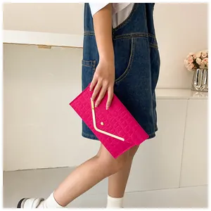 Close-up of bright fuchsia envelope clutch with crocodile texture and gold V-shaped metal trim