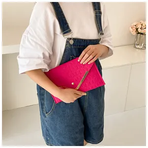 Detail of rose pink envelope clutch featuring crocodile pattern and gold V-shaped metal trim