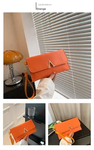 Detail view of orange crocodile pattern envelope clutch bag with gold V-shaped buckle